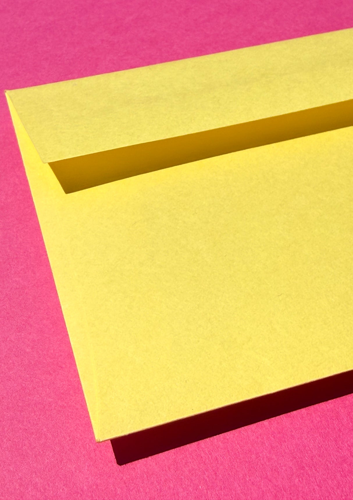 A bright yellow envelope showcasing the flap photographed on a vivid pink background.