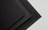 Stack of black cardstock sample sheets with a textured surface