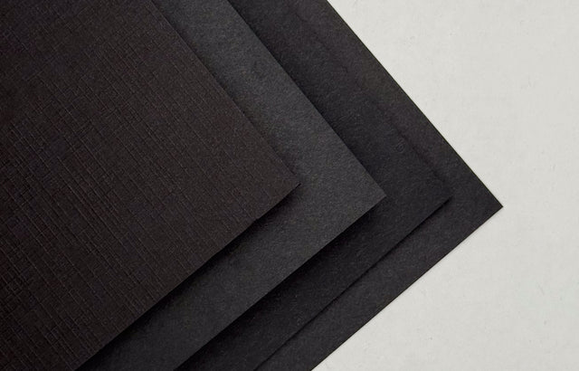 Stack of black cardstock sample sheets with a textured surface